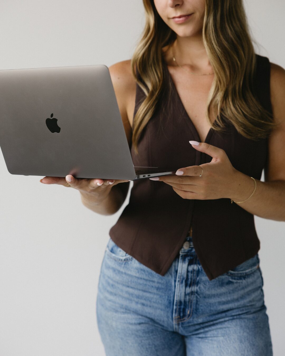 girl holding laptop to the side with a brown tank top vest on