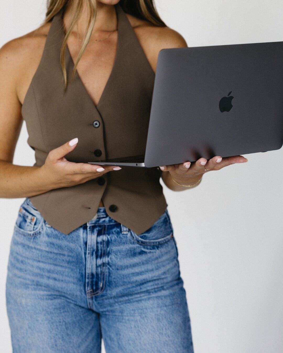 girl with long hair, wearing a dark olive green tank top vest holding a laptop to the side